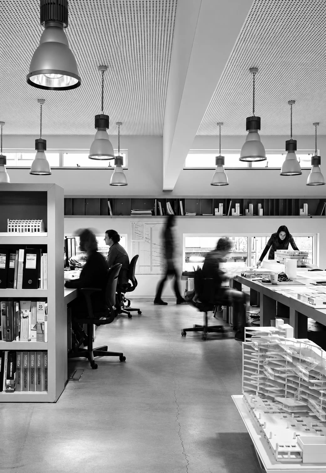 A black and white open-plan studio with people working at desks beside architectural models
