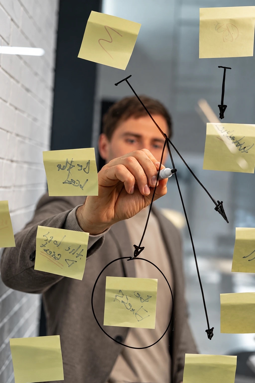 A person sketching arrows between sticky notes on a glass wall